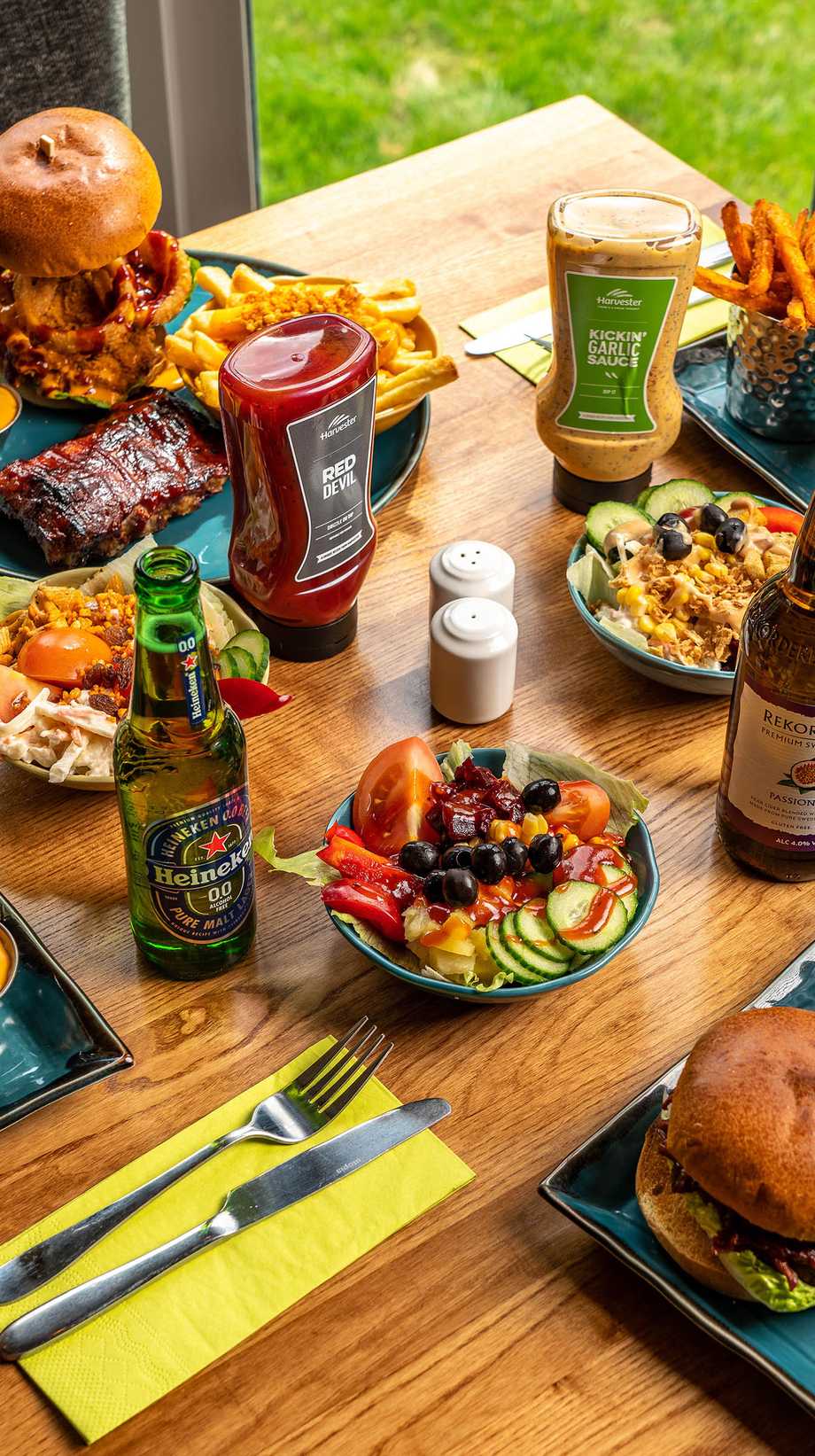 A table is covered with food and drinks, like burgers, salads, fries, and sauces.