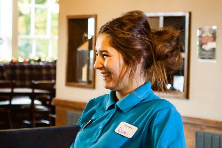 A team member with a blue shirt and a braid in her hair is smiling at a guest, off-camera.