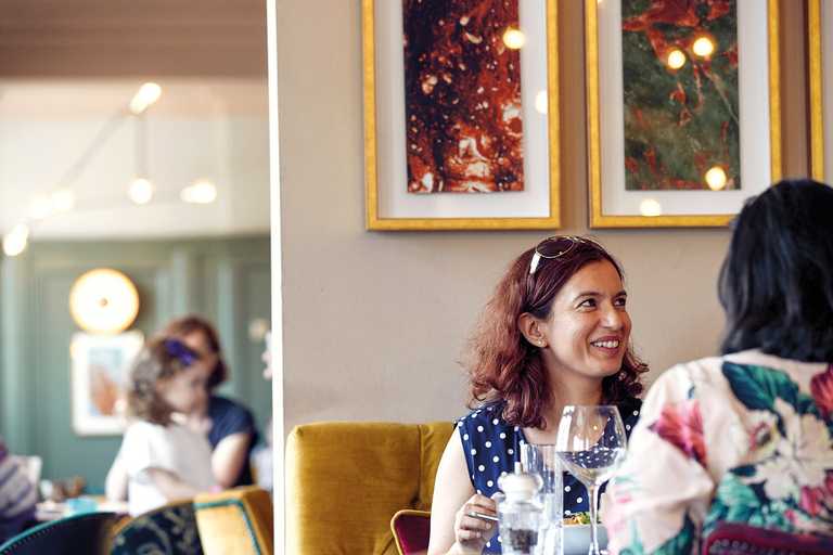 A guest smiles up at a team member who's off-camera. Behind her, artwork hangs on the wall.