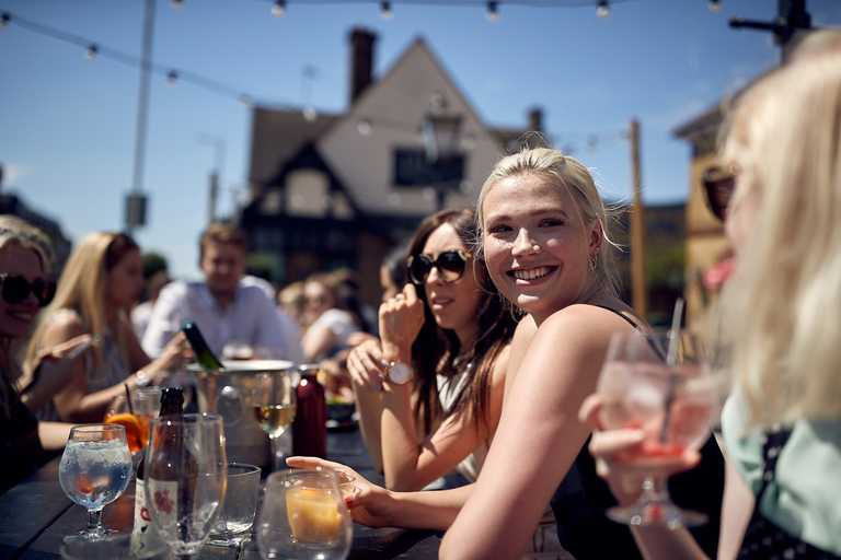 Friends smile at each other over drinks on a sunny day. In the background, a bottle is chilling in an ice bucket.