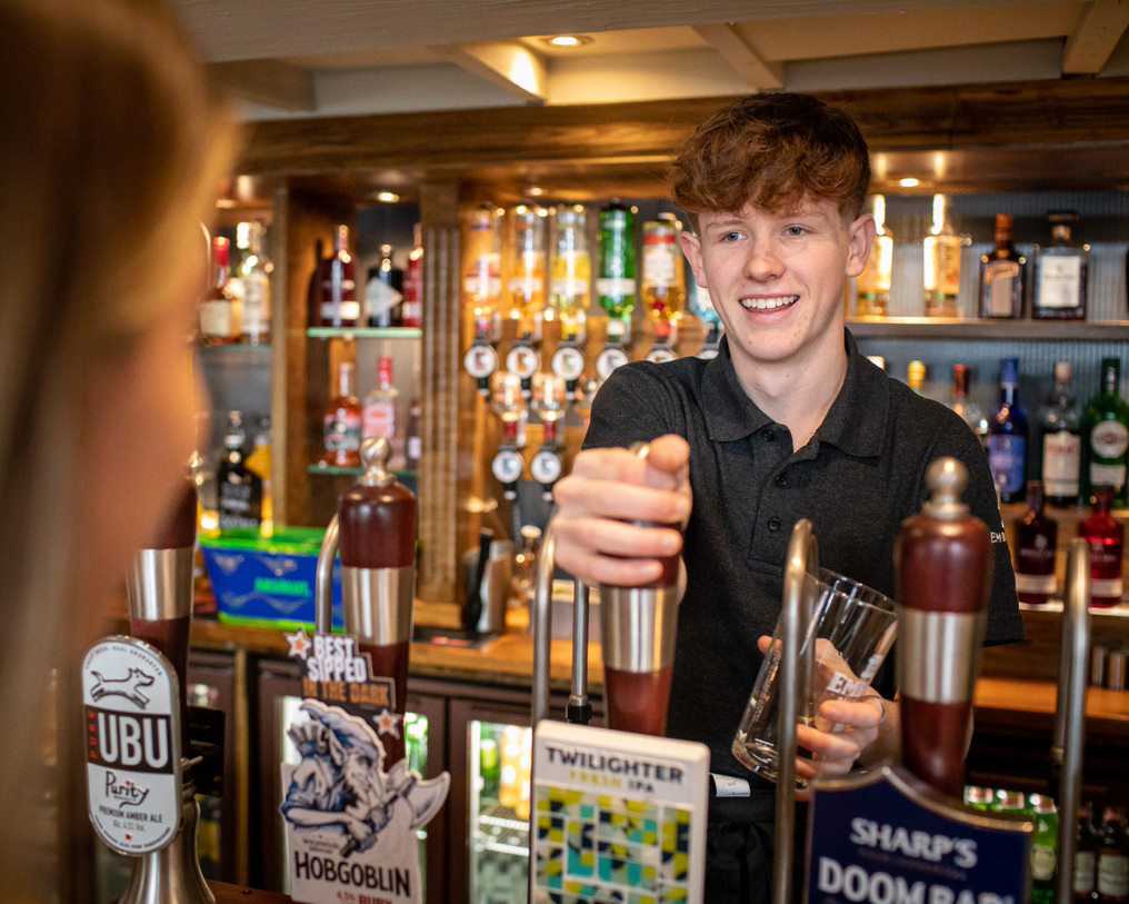 A team member reaches for a pint pull to serve a drink to a waiting guest.