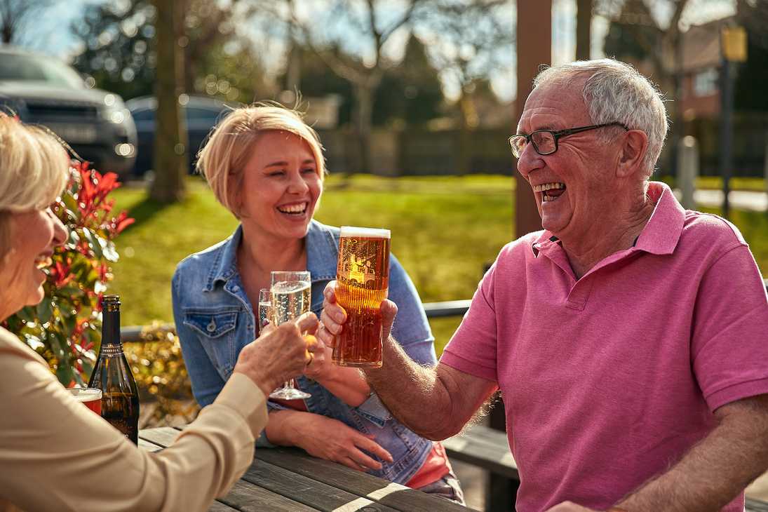 A man in a bright pink polo shirt laughs while raising a glass to the people sitting with him.