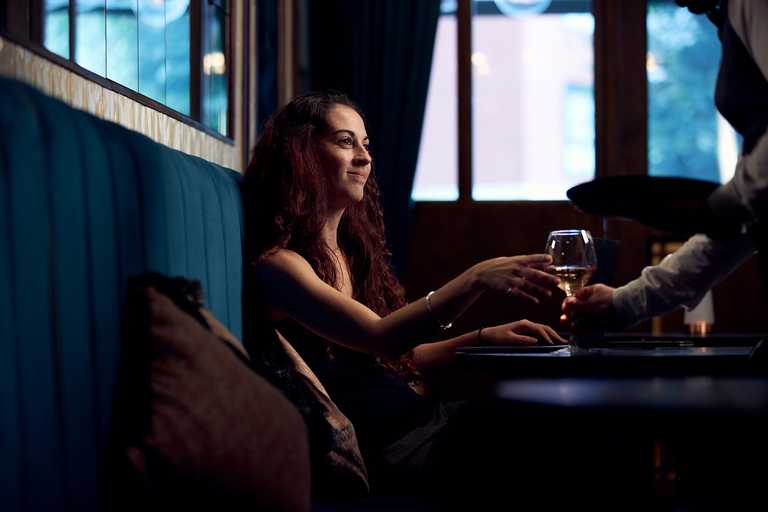 A guests smile at a team member as they reach for their drink, sitting in a deep blue booth.