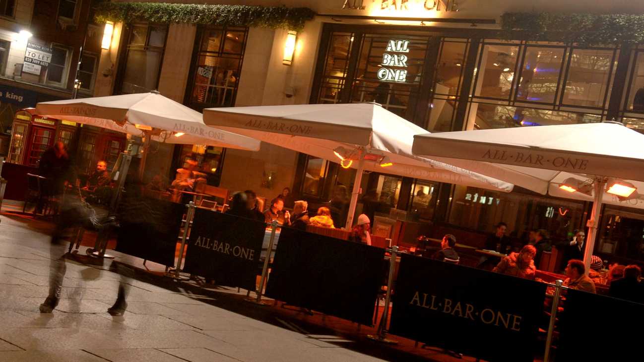 Tables and wide, white umbrellas are set up outside an All Bar One, where guests are sitting.