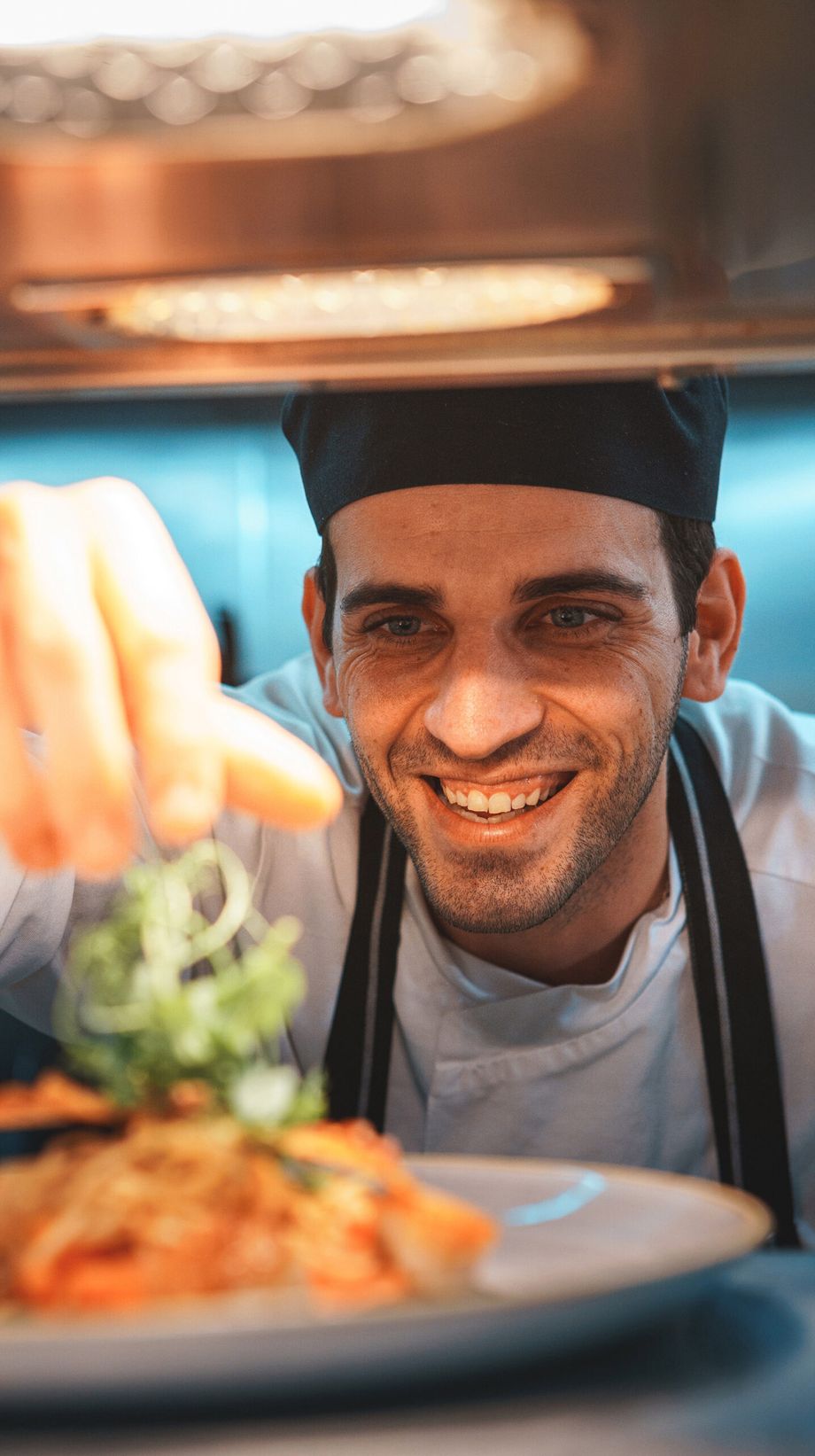 A chef sprinkles spring onions on a fresh plate of scallops.