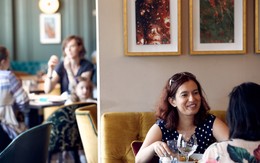 In the foreground, two guests laugh over glasses of wine. In the background, a family is sitting around a table.