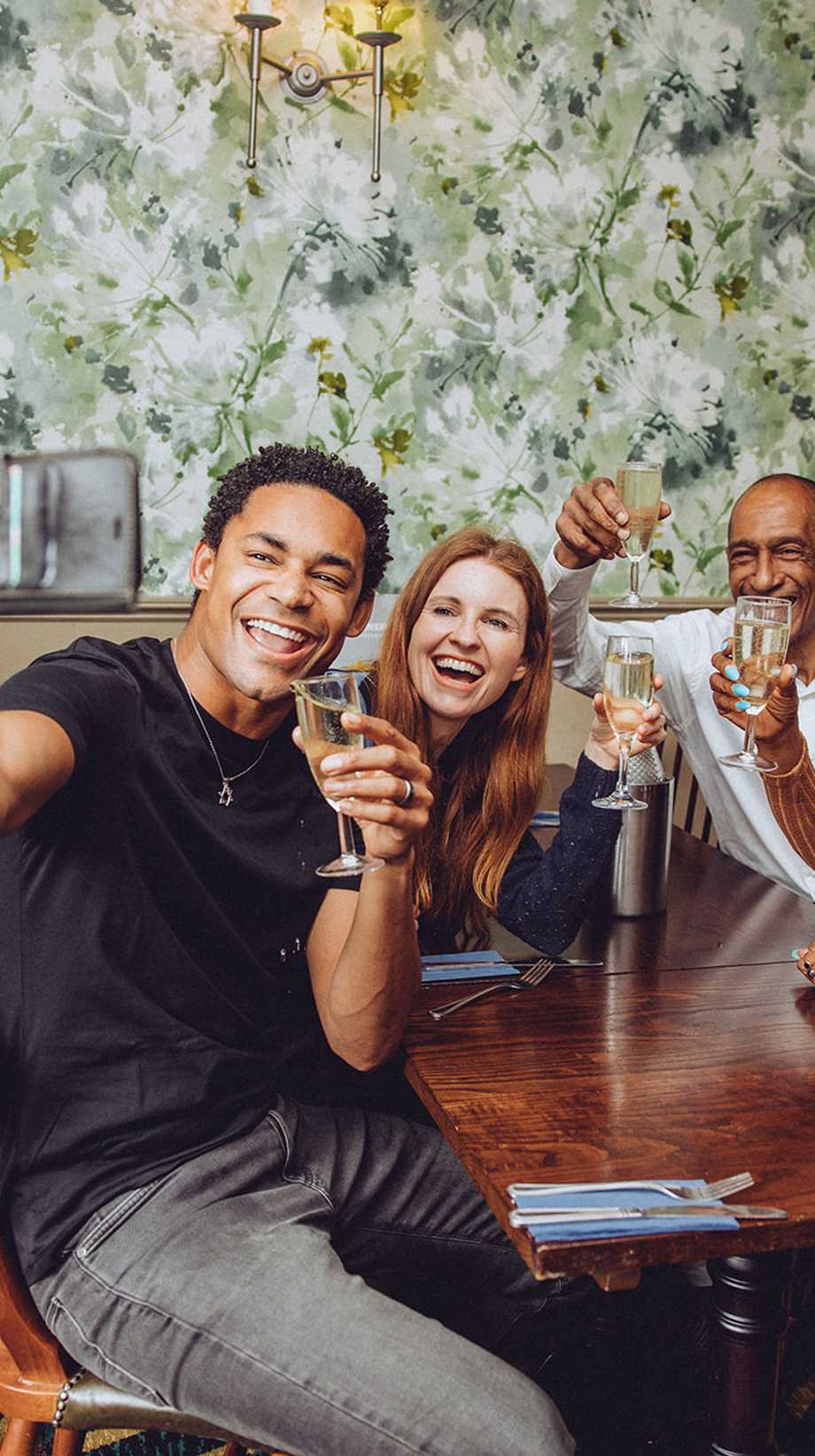 A group of friends drinking are taking a selfie against a patterned wall.