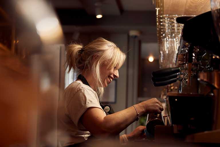A laughing barista preparing a drink at a coffee machine.