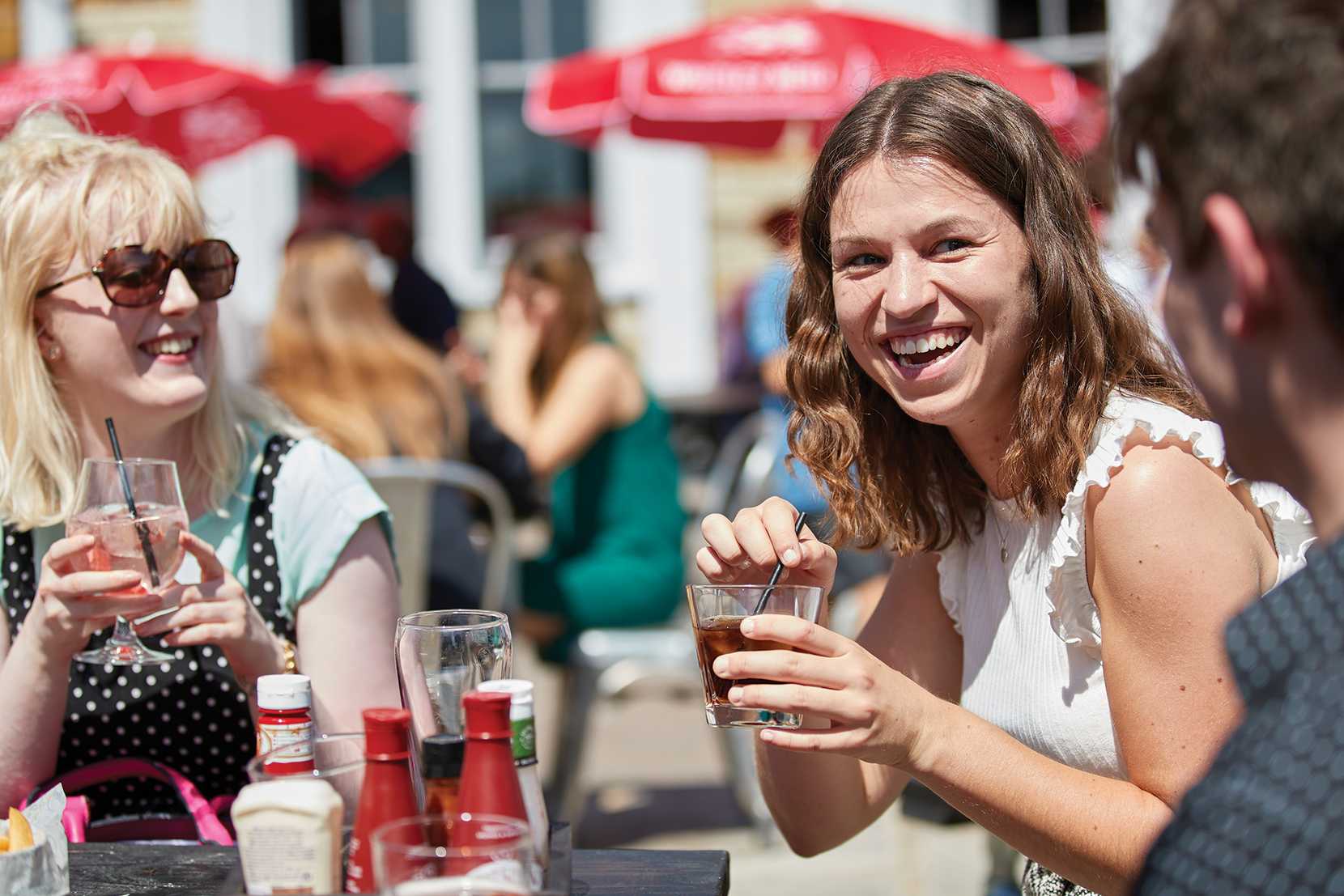 Friends smile and laugh over spirits and mixers, with a selection of condiments in the foreground.