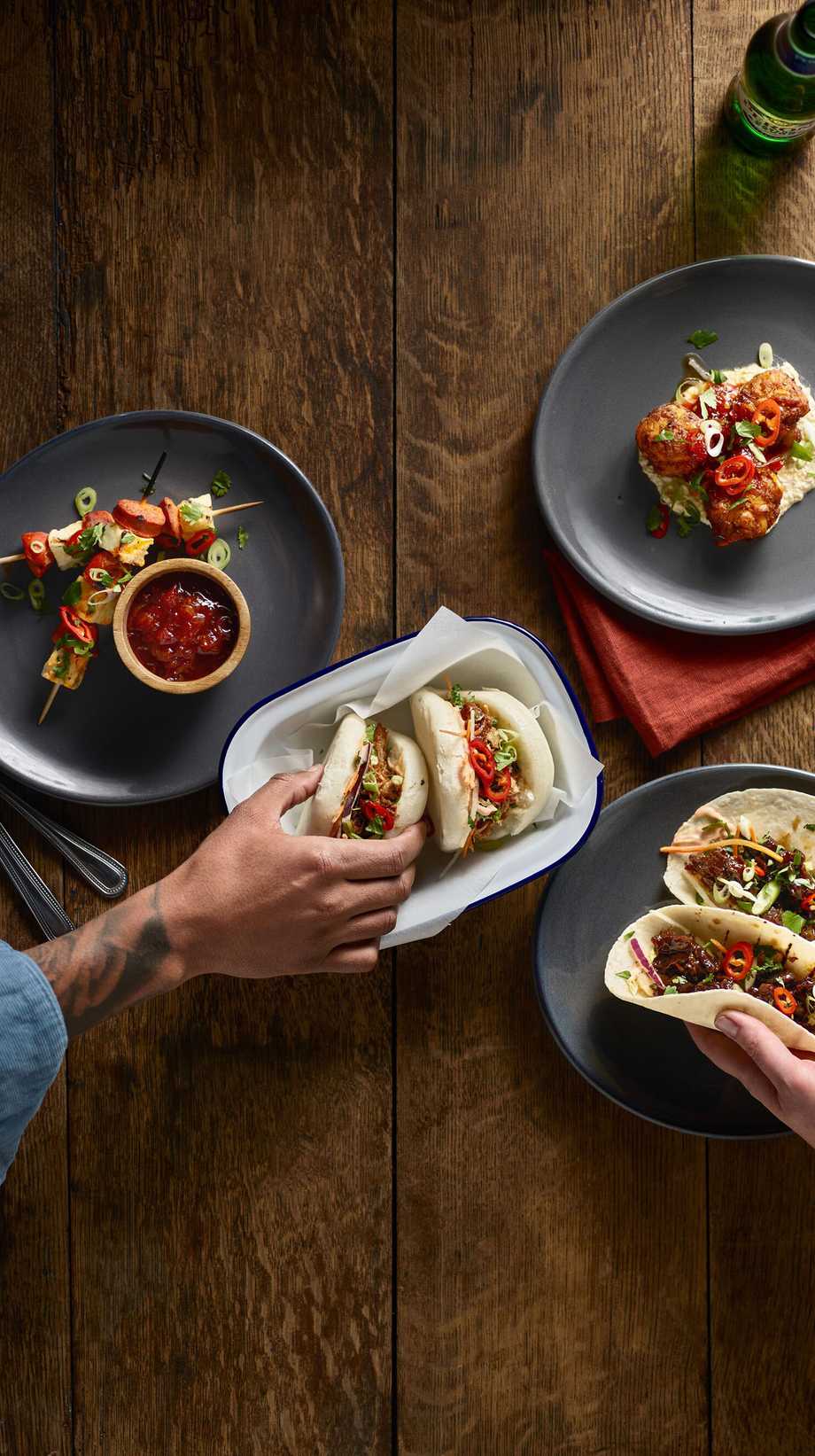 Two hands are reaching in to pick up tapas dishes, seen from a birds-eye view.