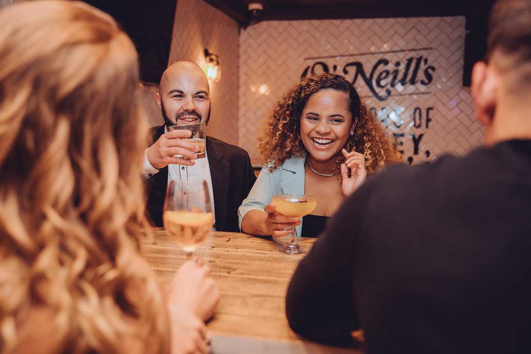 Staring over the shoulders of two guests, we see two guests holding their drinks and laughing.