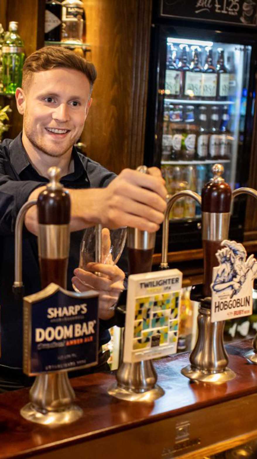 A team member behind the bar smiles at a guest while pulling them a fresh pint.