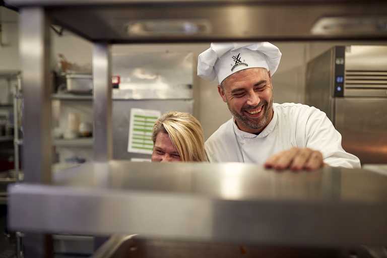 A chef and his co-worker are laughing in a kitchen.