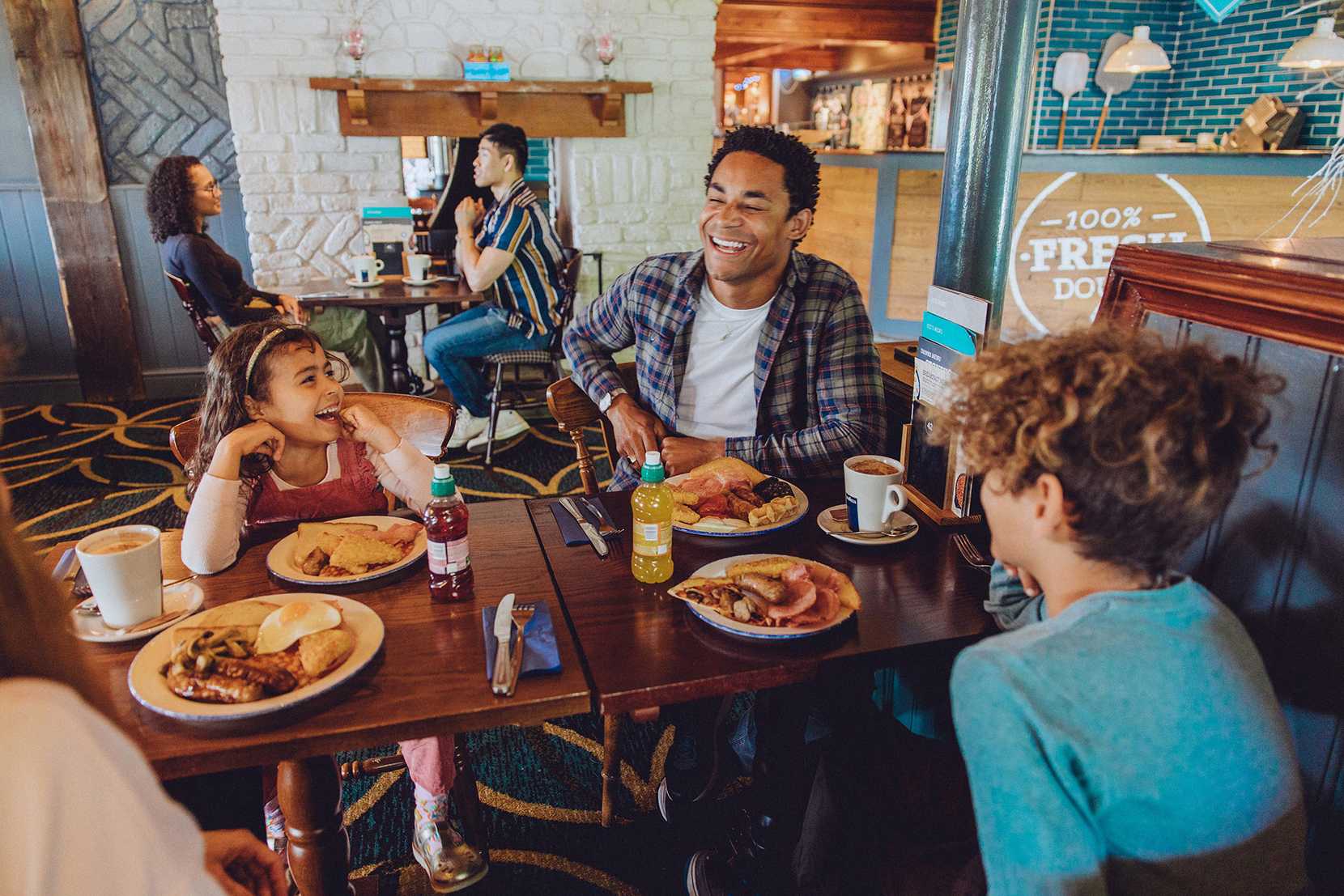 A family sit around a table laughing. On the table, there is a wide range of food and drinks.