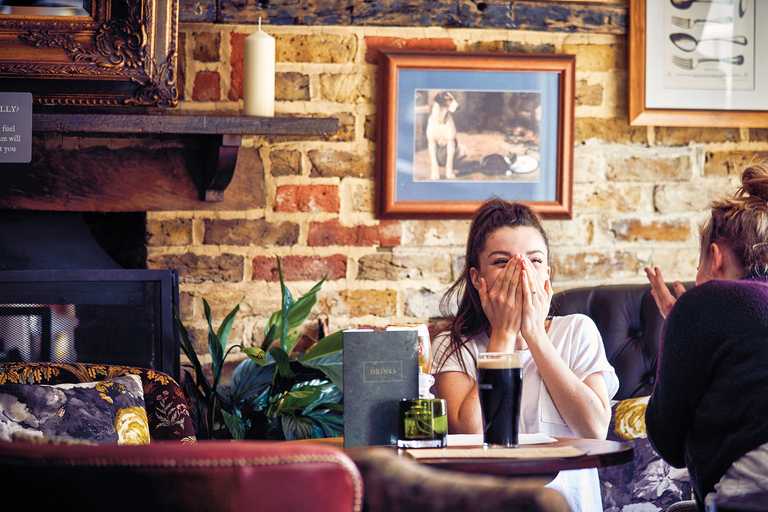 A woman is enjoying a drink with her friend, hands covering her face.