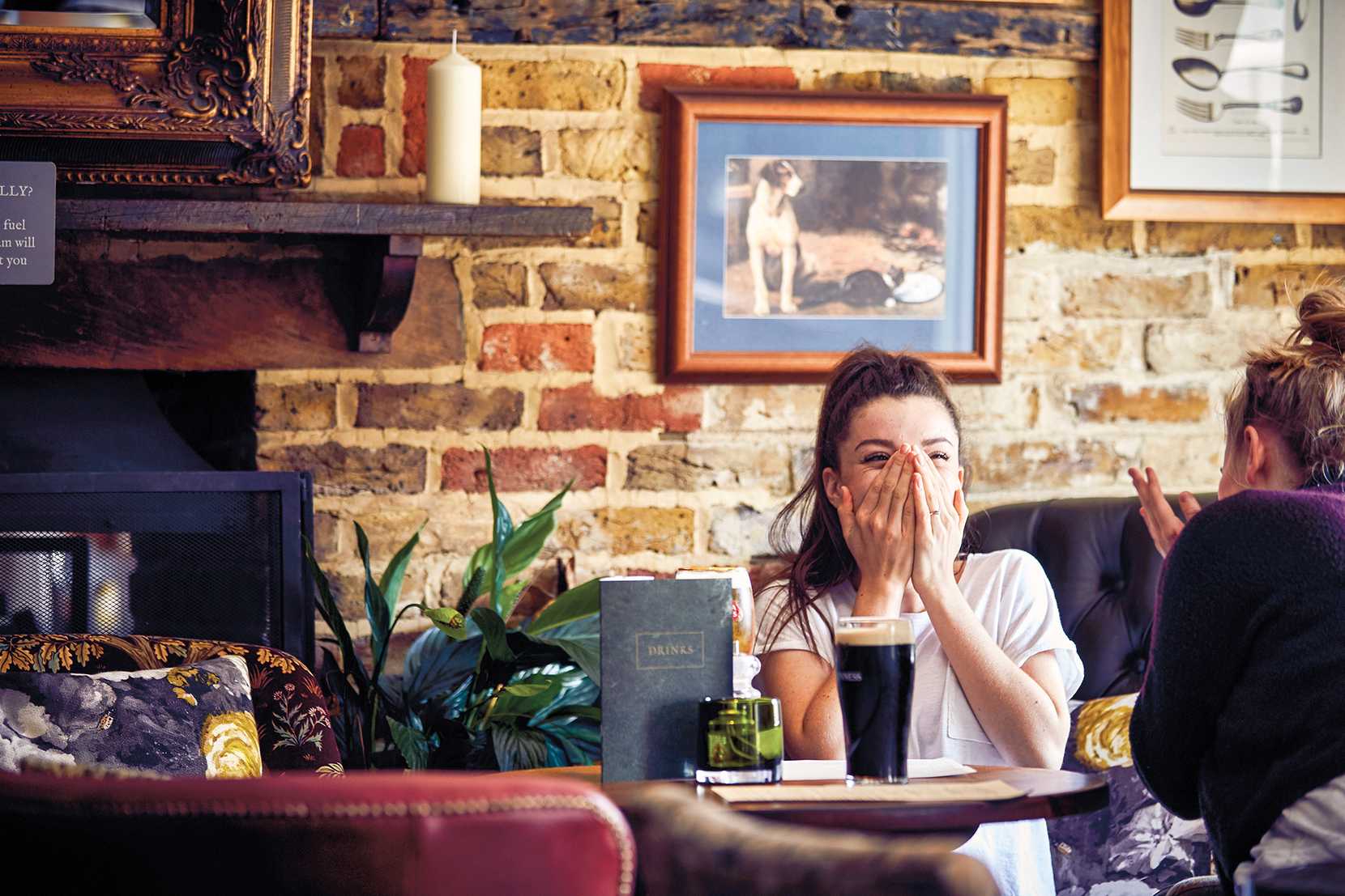 A woman is enjoying a drink with her friend, hands covering her face.