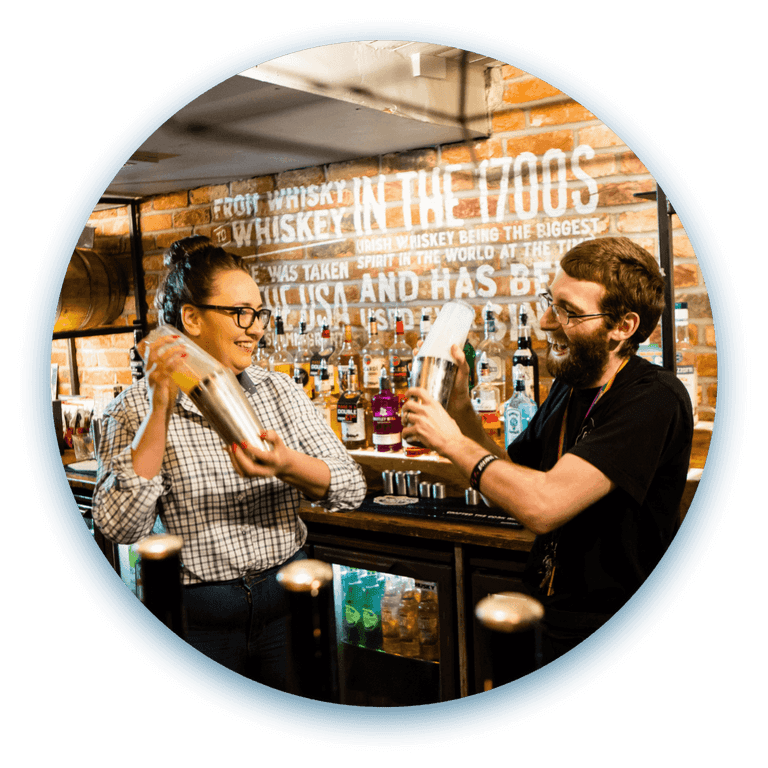 Two team members behind the bar mix cocktails while smiling.