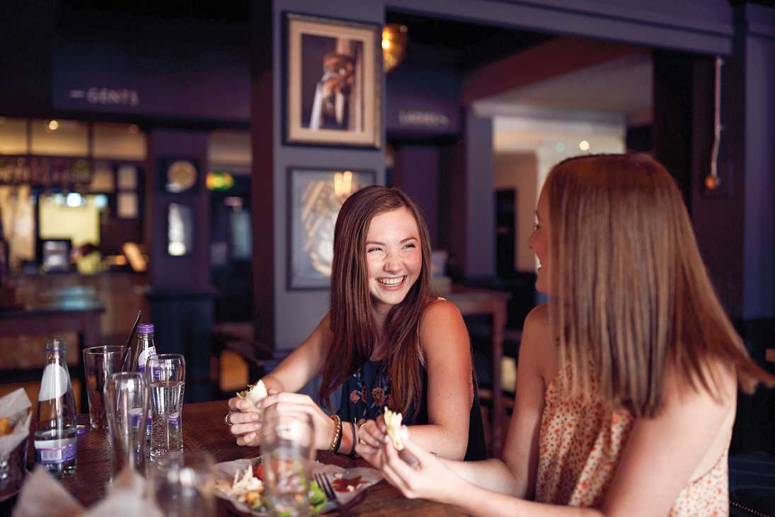Two women laughing together over lunch and drinks.
