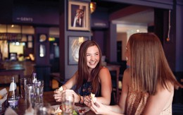 Two women laughing together over lunch and drinks.