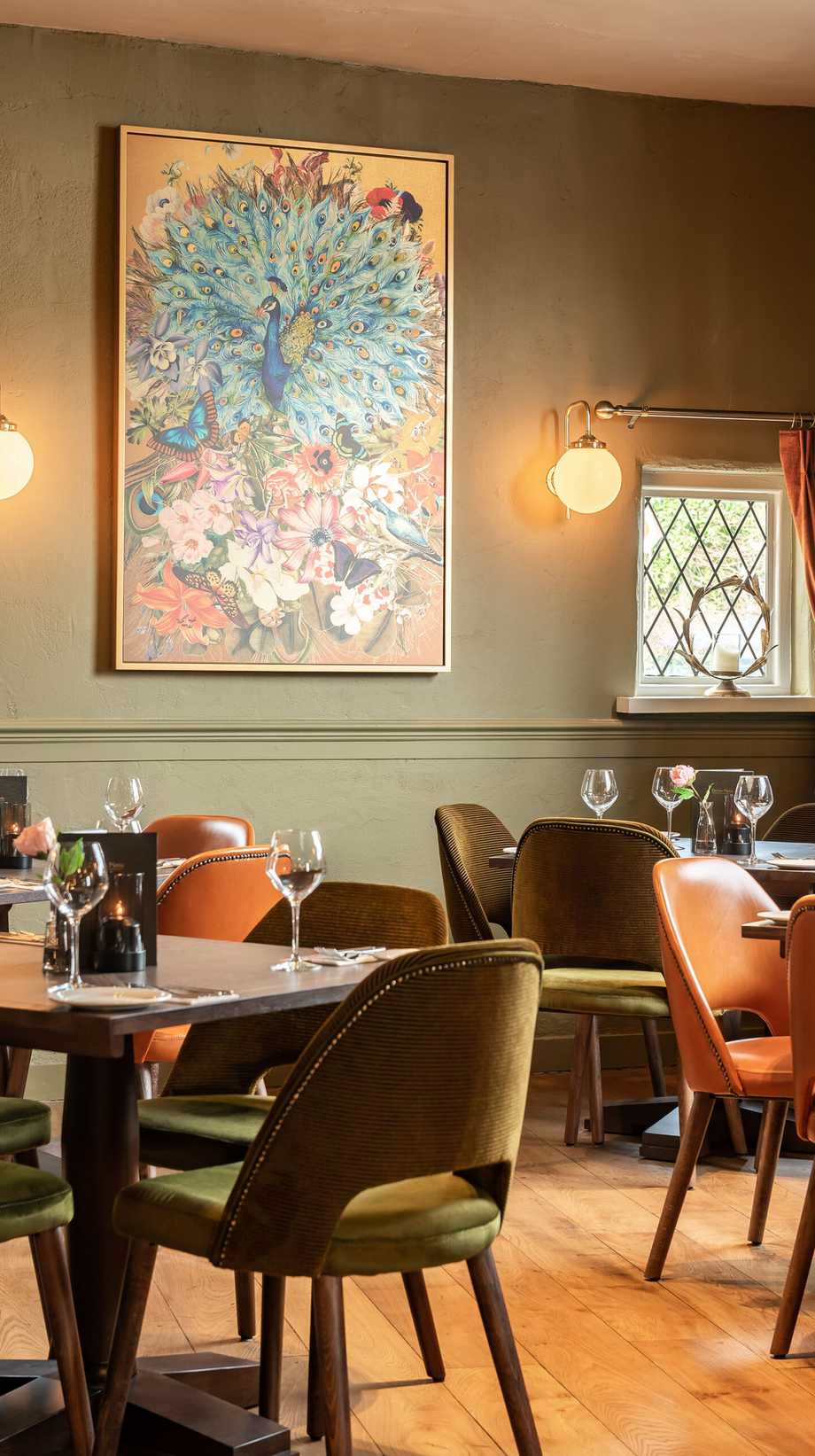 An empty pub awaits guests with soft lighting, eye-catching floral artwork, and dark green walls.