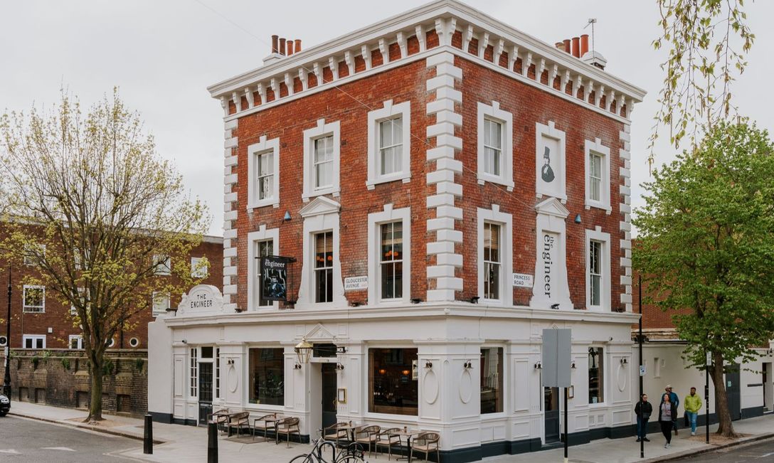 The Engineer pub, a red-brick, three-storey corner building with white accents and large windows. Bicycles are parked out front and pedestrians walk nearby, creating a welcoming streetscape.