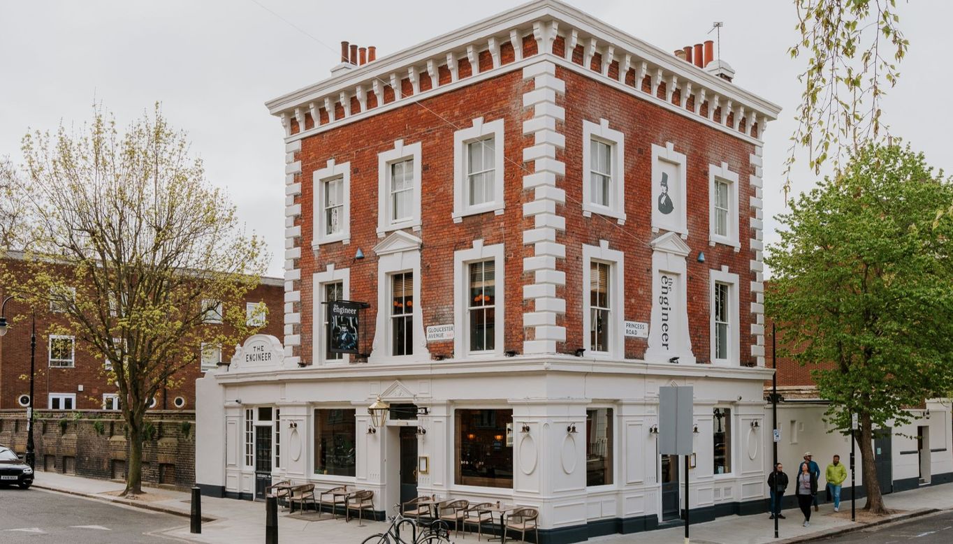 The Engineer pub, a red-brick, three-storey corner building with white accents and large windows. Bicycles are parked out front and pedestrians walk nearby, creating a welcoming streetscape.