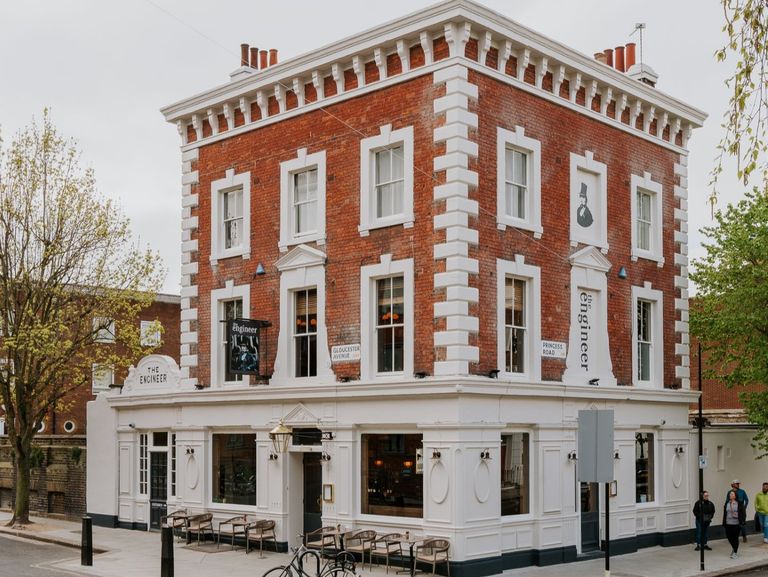 The Engineer pub, a red-brick, three-storey corner building with white accents and large windows. Bicycles are parked out front and pedestrians walk nearby, creating a welcoming streetscape.
