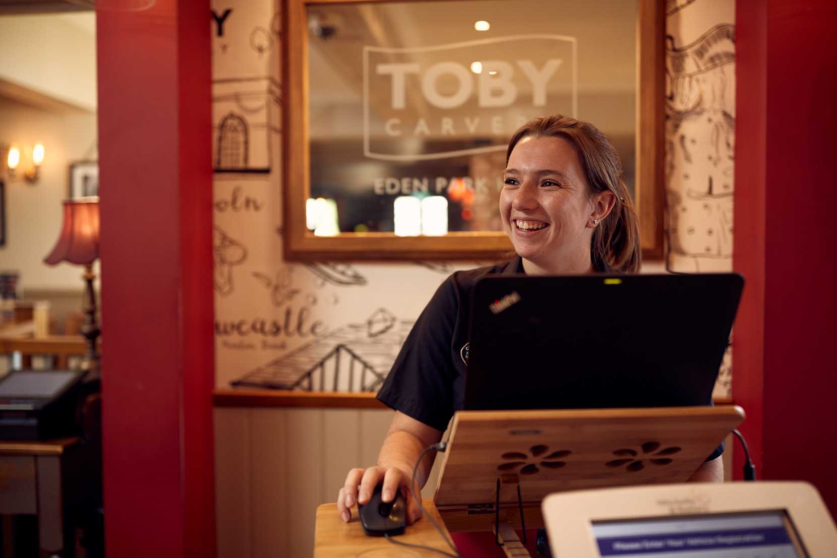 A team member at Toby Carvery stands smiling, ready to greet guests at the door.