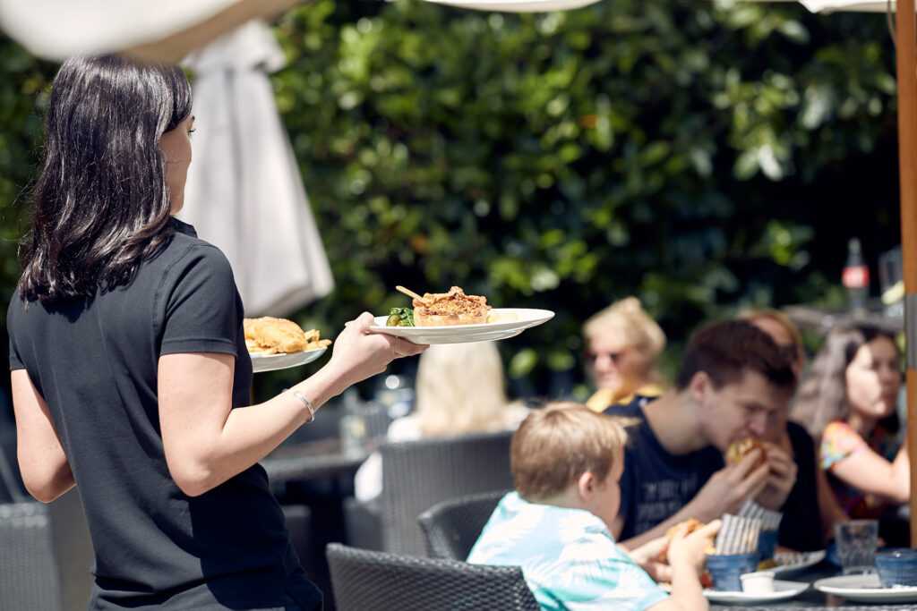 A team member is delivering two plates to guests sitting outside.