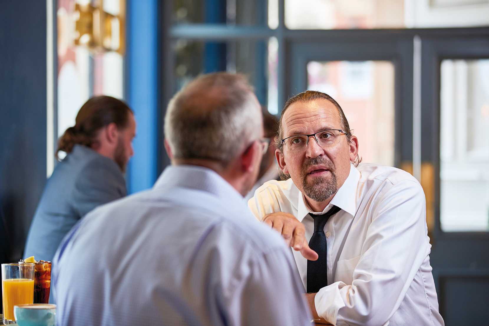 Two men in shirts are in deep conversation. Next to them, there are two soft drinks and a mug.