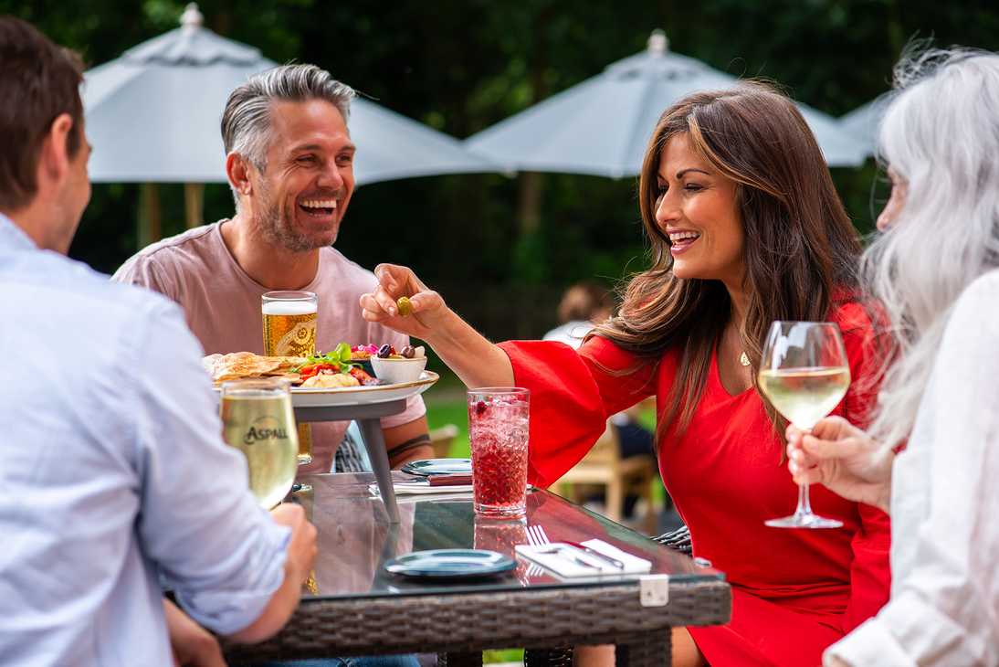 Four friends are eating and drinking outside, laughing together.