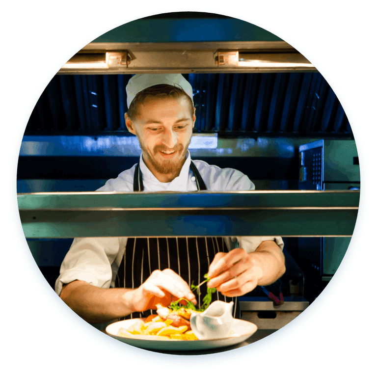 A chef in a white shirt, white hat, and striped apron adds the finishing details to a dish.