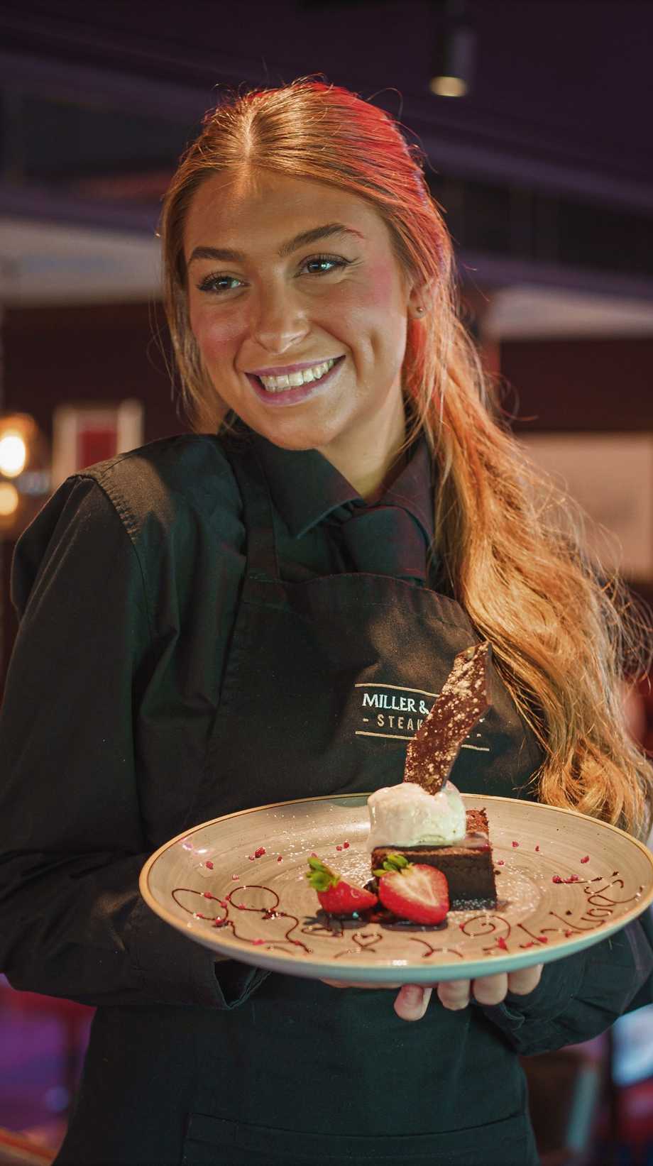 A team member serves a dessert to a waiting guest, off-camera.