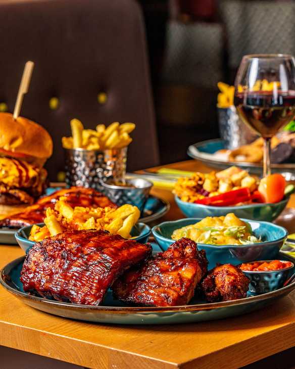 Food is all laid out on a table, including steak, burger, fries, sides, and drinks.