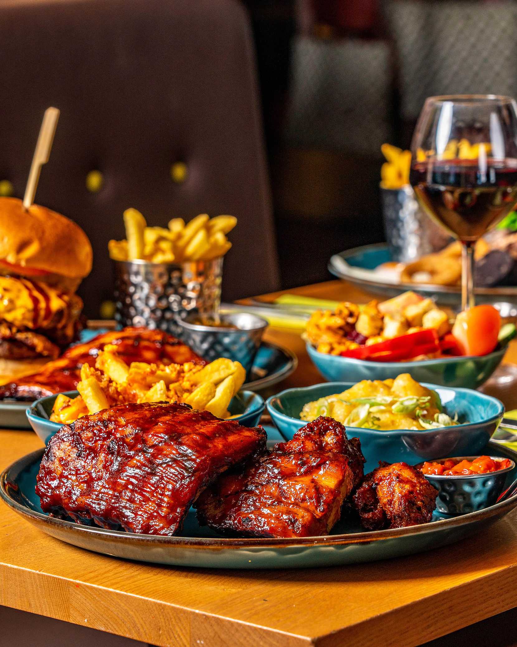 Food is all laid out on a table, including steak, burger, fries, sides, and drinks.