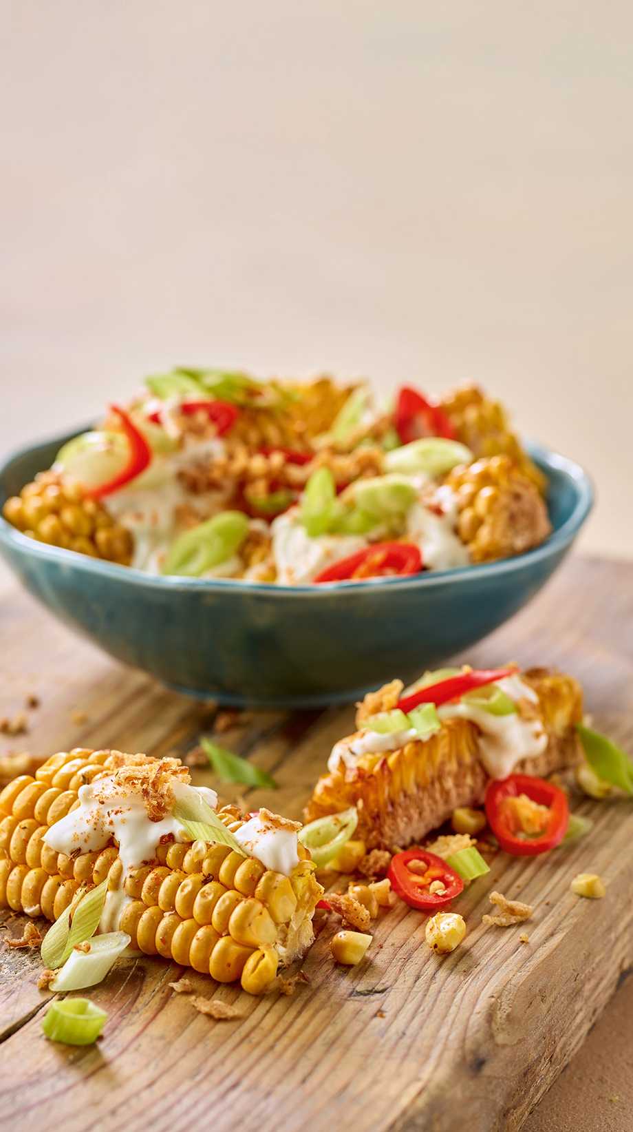 A pasta salad starter in a blue bowl sits on top of a wooden block. Around its base, pasta, lettuce, and tomatoes are scattered about.