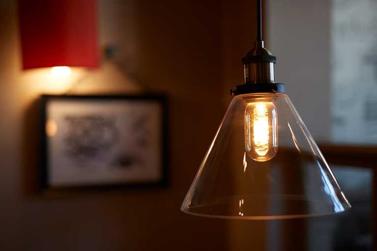 A hanging pendant light creates a cosy atmosphere in a pub or restaurant, with out-of-focus art hanging on the wall behind it.