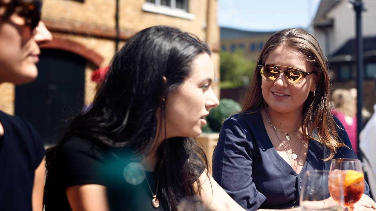 A group of friends are chatting over Aperol Spritz in a sunny beer garden.