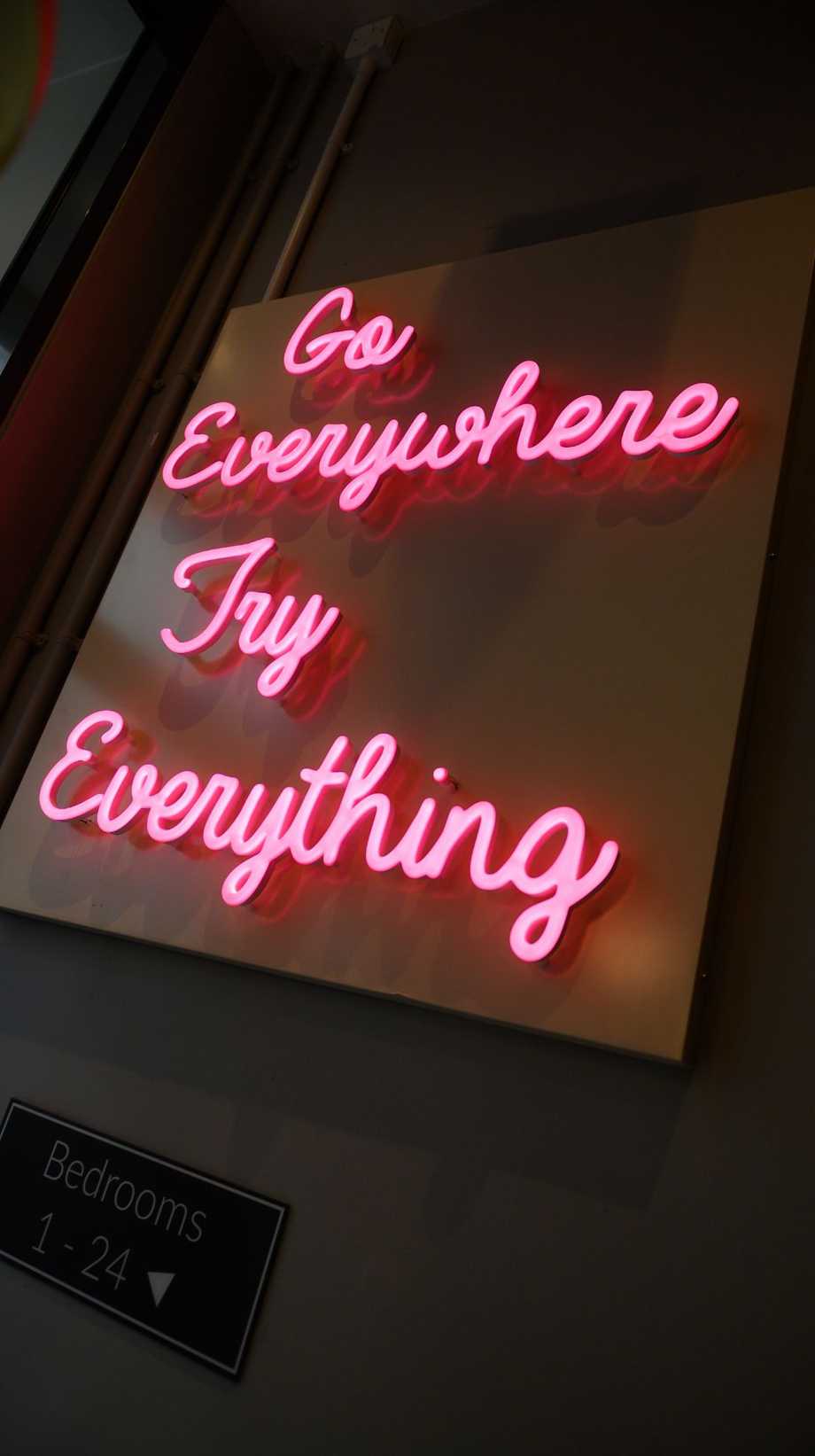 A pink neon sign says, "Go everywhere. Try everything."