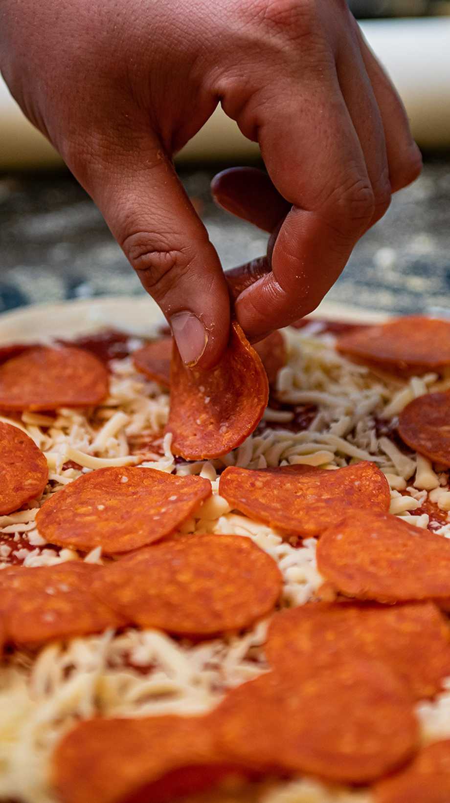 A chef places pepperoni onto a pizza base of tomato and cheese.