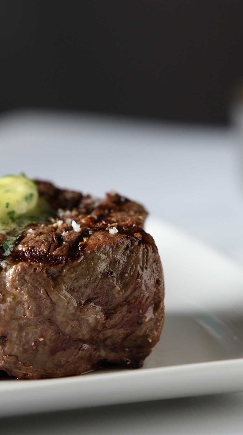 Butter is melting on top of a thick cut of steak, resting on a white plate.