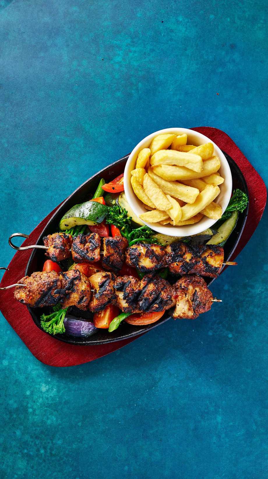 A bird's eye view of a jerk chicken skewer skillet, complete with chips and grilled vegetables.