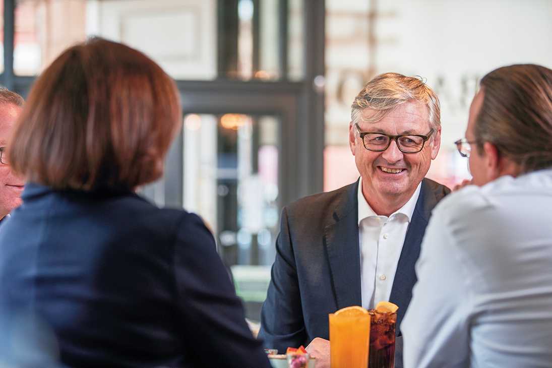 A table of smartly-dressed guests chat over drinks, each with a garnish of orange floating on top.