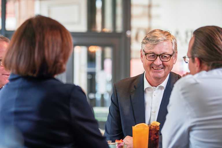 A table of smartly-dressed guests chat over drinks, each with a garnish of orange floating on top.