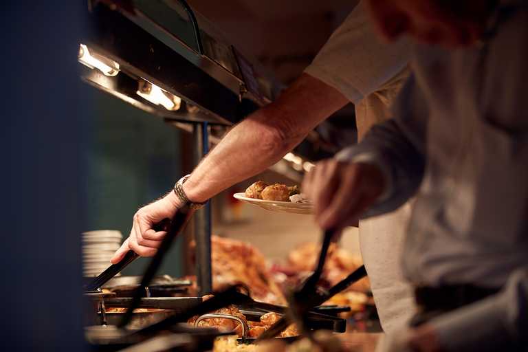 A man is serving himself at the carvery deck. On his plate, there are some crispy roasts waiting.