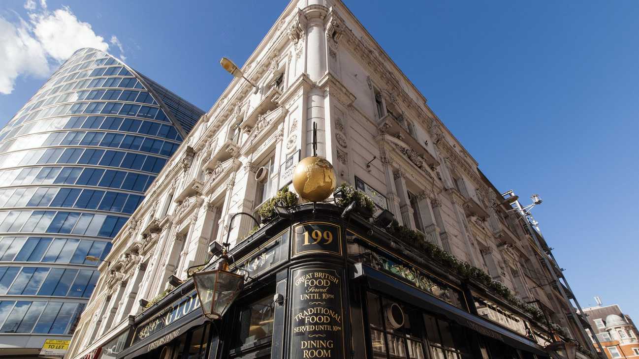 An exterior shot of The Globe pub, angled upwards, contrasting with a modern, glass building and blue sky.